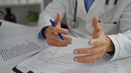 Doctor's hands gesturing during a discussion in a clinic room with visible documents and pen signifying a medical consultation or meeting setting inside a healthcare workplace.