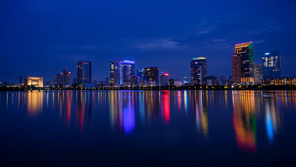 Naklejka premium Illuminated city skyline reflected in dark water at night buildings skyscrapers