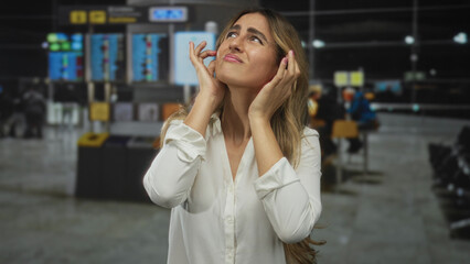 Young blonde woman in white blouse covers ears with hands in a store checkout area; stress...