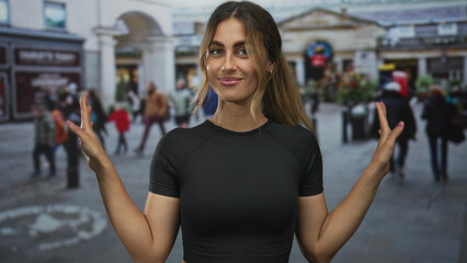 Fototapeta premium Young blonde woman shows bare arms in open palm shrug gesture in a crowded street; openness confidence.