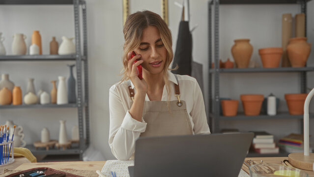 Young blonde woman holds phone in a pottery studio; creativity entrepreneurship concentration inspiration.