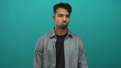 Young hispanic man in casual attire stands in front of an isolated vibrant green background, expressing a pensive and relaxed demeanor with closed eyes and neutral expression.