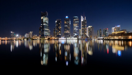 Fototapeta premium Illuminated city skyline reflected in dark water at night cityscape urban