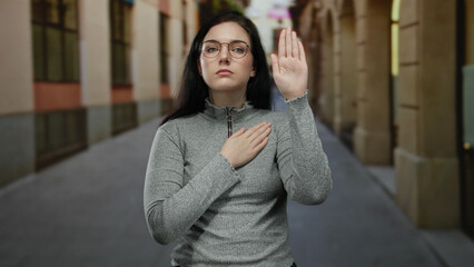 Woman making oath gesture on quiet street wearing glasses shows serious commitment outdoors