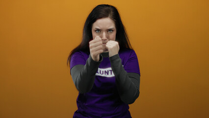 Woman in purple volunteer shirt posing with fists raised against orange background showing...