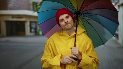 Man in yellow raincoat holds colorful umbrella on city street