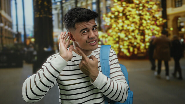 Young man gestures quizzically against a backdrop of city lights in an urban street scene, highlighting an intriguing expression and casual fashion in a nighttime environment.