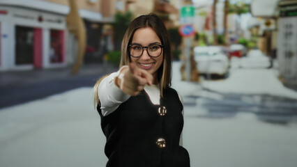 Woman pointing energetically with finger in a vibrant outdoor street setting wearing glasses and...