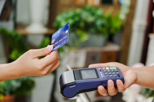 Closeup of credit card held in hand during contactless payment to senior asian florist showing card reader inside plant filled flower store symbolizing modern small business transaction
