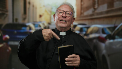 Elderly priest holding a book gestures while standing on a busy street lined with cars, implying a...