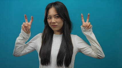 Chinese woman making quotation gesture over blue background, expressing concept or humor while...