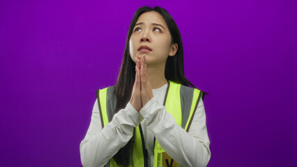 Chinese woman in reflective vest stands in a prayerful pose against a vibrant purple background,...