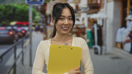 Woman flexing arm with a smile holds yellow clipboard on a busy street showcasing confidence and...