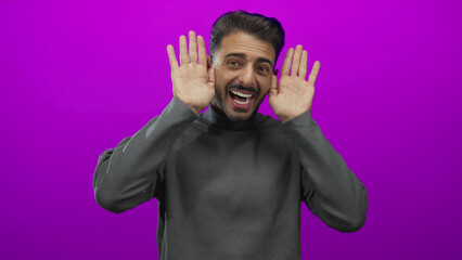 Young hispanic man wearing a grey turtleneck smiling raises hands with open palms in studio;...