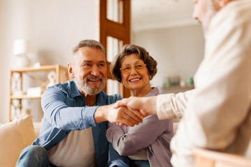 Satisfied senior spouses making sale purchase deal, handshaking with real estate agent agreeing to...