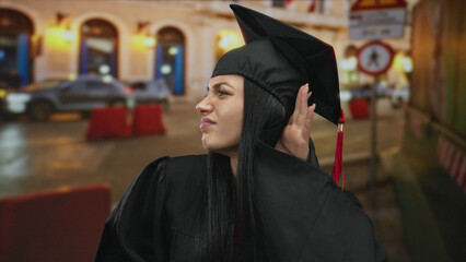 Graduated woman in cap and gown listens intently on a busy city street, blending urban vibrancy...