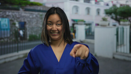 Young woman in blue shirt smiling and pointing on city street with urban background, highlighting...