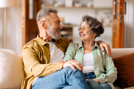 Happy loving senior couple embracing and enjoying pleasant conversation, sitting on sofa at home. Happiness in retirement and marriage