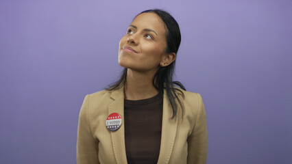 Young hispanic woman wearing an i voted badge smiles confidently against a vibrant purple...