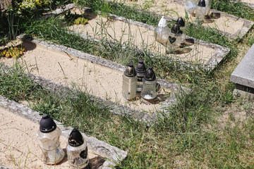 Old neglected graves with sand surface. Weathered cemetery with candles and overgrown grass....
