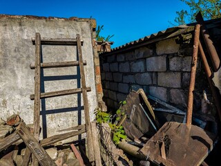 A wooden ladder leaning against a brick wall. The ladder is old and rusted. The wall is made of bricks and has a metal roof. The scene is somewhat abandoned and gives off a feeling of neglect