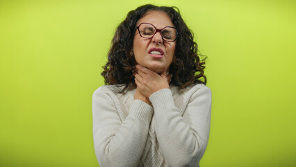 Middle-aged woman with curly hair in discomfort holds neck against isolated yellow background,...