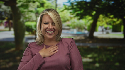 Woman laughs and points finger toward camera amid green trees and sunlight in forest setting;...