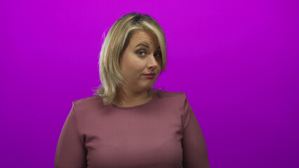 Young blonde woman wearing mauve top with hair framing face tilts head and raises eyebrow in...