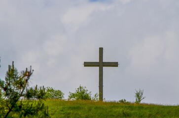 A large cross is standing in a field of grass. The sky is cloudy and the sun is not visible