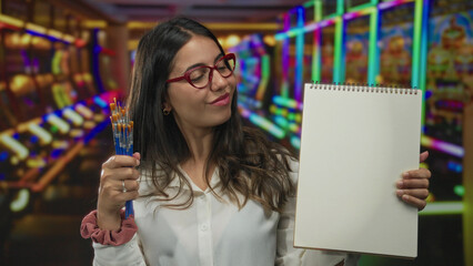 Woman artist holding pencils and notebook in vibrant casino setting with slot machines, displaying...