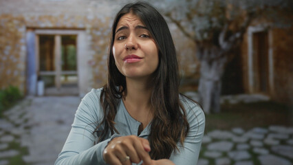 Young hispanic woman finger tapping her palm outdoors by aged stone building pressing for cash...