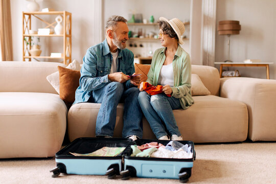 Senior European tourists couple packing clothing and travel essentials for awaited vacation, preparing for trip
