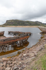 Rusted wooden and metal shipwrecks partially submerged in shallow coastal waters against a backdrop...