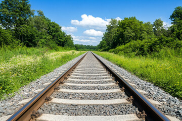 Fototapeta premium Railway tracks converge into the distance under a sunny sky