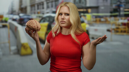 Woman holding brain in construction site, looking confused amidst busy city backdrop with traffic.