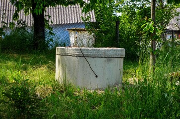 Fototapeta premium A cement basin with a white bucket on top of it. The bucket is dirty and has a few leaves in it. The basin is surrounded by grass and trees