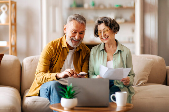 Happy senior couple with laptop and papers planning family budget together, calculating spends and taxes on retirement, sitting on couch