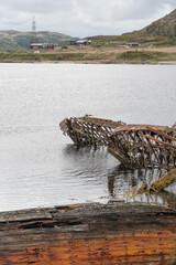 Rusted wooden and metal shipwrecks partially submerged in shallow coastal waters against a backdrop...