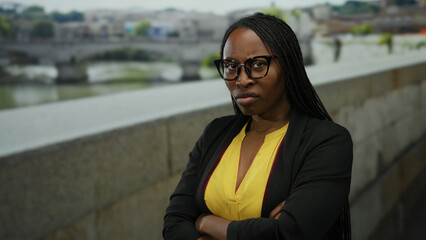 Woman standing outdoors with arms crossed wearing a yellow shirt and glasses on an urban street...