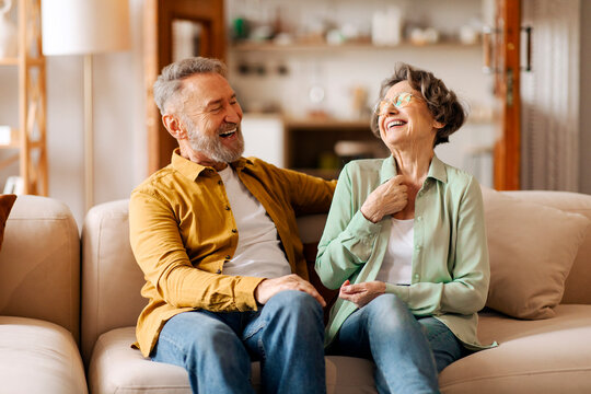 Elderly husband and wife having fun, talking, laughing, enjoying conversation and happy retirement, relaxing on couch at home