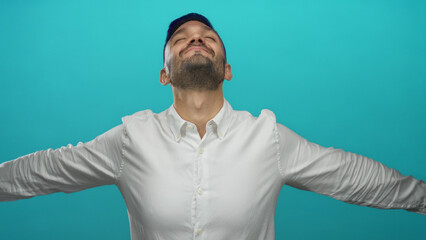 Young man expressing joy with arms raised and eyes closed against a vibrant blue background,...