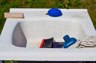 A sink with a brush and a bottle of cleaner on it. The sink is dirty and the brush is old