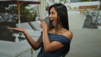 Woman in blue dress giving thumbs up and pointing at palm while standing outdoors suggesting...