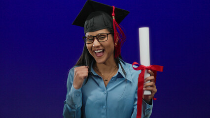 Graduated woman celebrating with diploma over an isolated blue background, showcasing joy and...