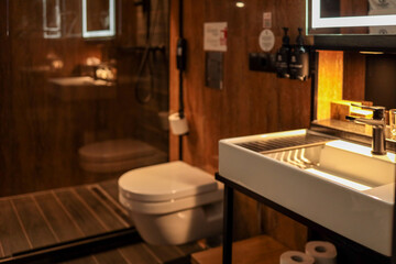 Modern hotel bathroom interior with white sink, toilet, glass shower cabin, illuminated mirror and...