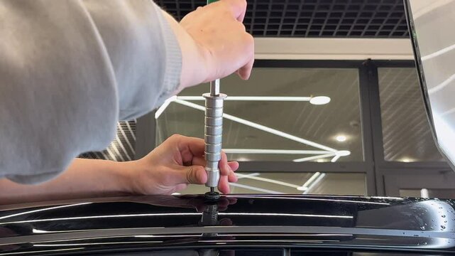 PDR. Process of paintless dent repair on car body. The mechanic at the auto shop with tools to repair dents in car body. Body repair. A specialist repairs a dent on the car body without painting.