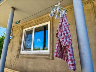 A plaid shirt is hanging on a clothesline outside. The shirt is red and white. The clothesline is...