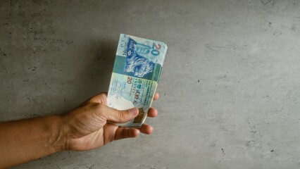 Hand holding hong kong dollars against a concrete wall background, showcasing currency, money, and...