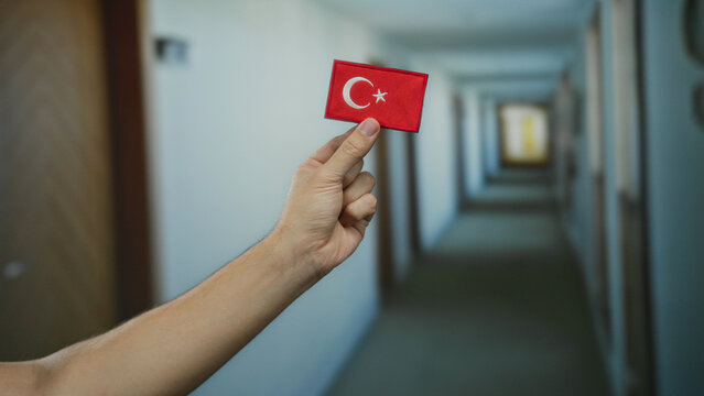 Caucasian man holding turkish flag patch in a hotel corridor illustrates cultural identity indoors. - Powered by Adobe
