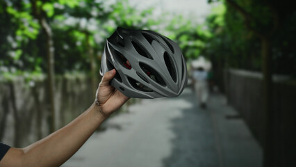 Man holding helmet outdoors on a city street with blurred trees in the background, highlighting...